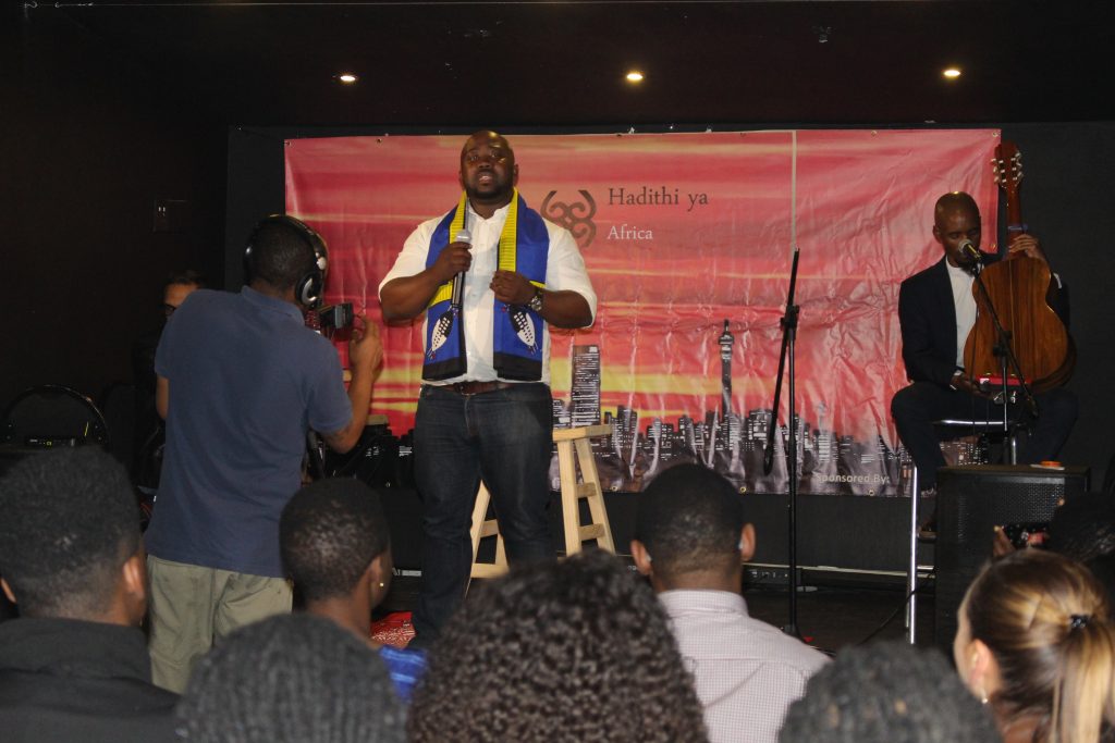 Thandwefika Tshabalala speaking on stage at Hadithi ya Africa, photographed from the back of the room over the heads of the audience