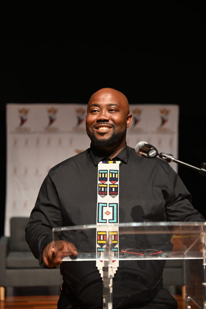 Thandwefika Tshabalala speaking from a lectern, mid smile, at a formal event