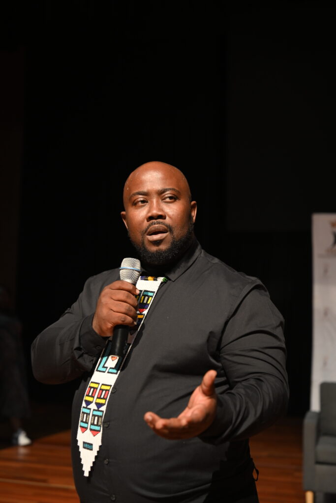 Thandwefika Tshabalala with a microphone, one arm open to the room